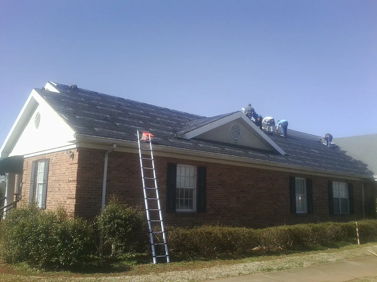 Crew tearing shingles off a brick ranch roof with a ladder set — Emergency Roof Repair work by our crew in White Sulphur Springs