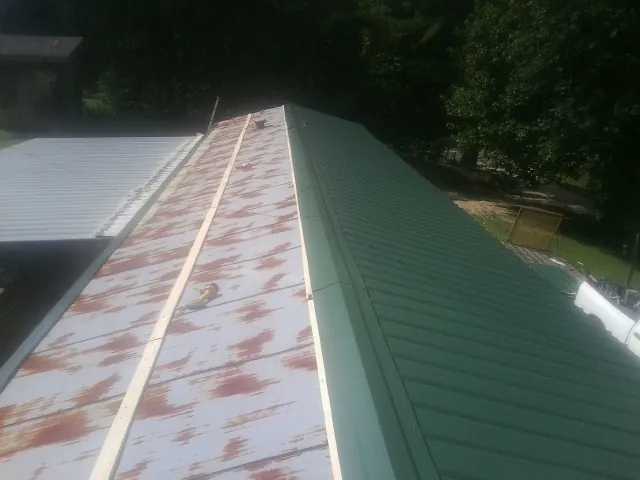 Old rusted panels beside newly installed green metal roofing — Wind Damage Roof Repair by Roofing Brothers in White Sulphur Springs