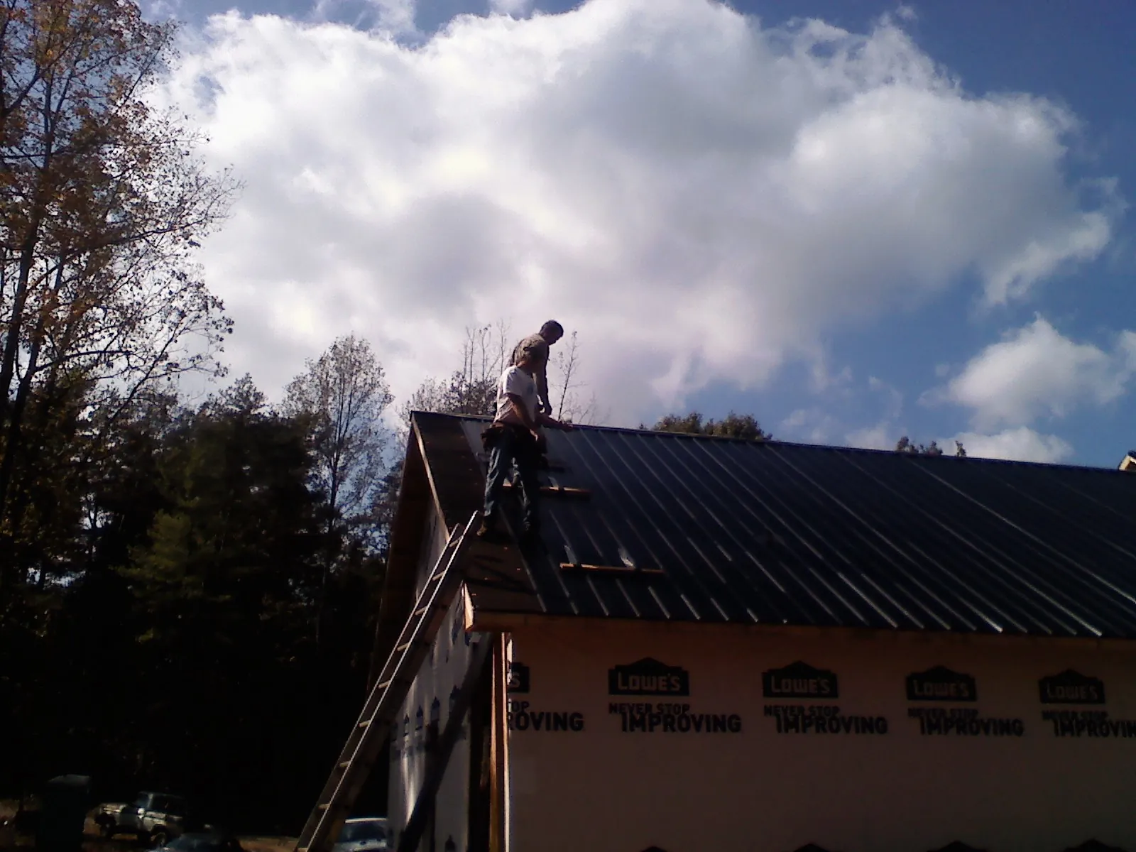 Roofer fastening dark metal panels high against a cloudy sky, from a Roof Inspection job in White Sulphur Springs