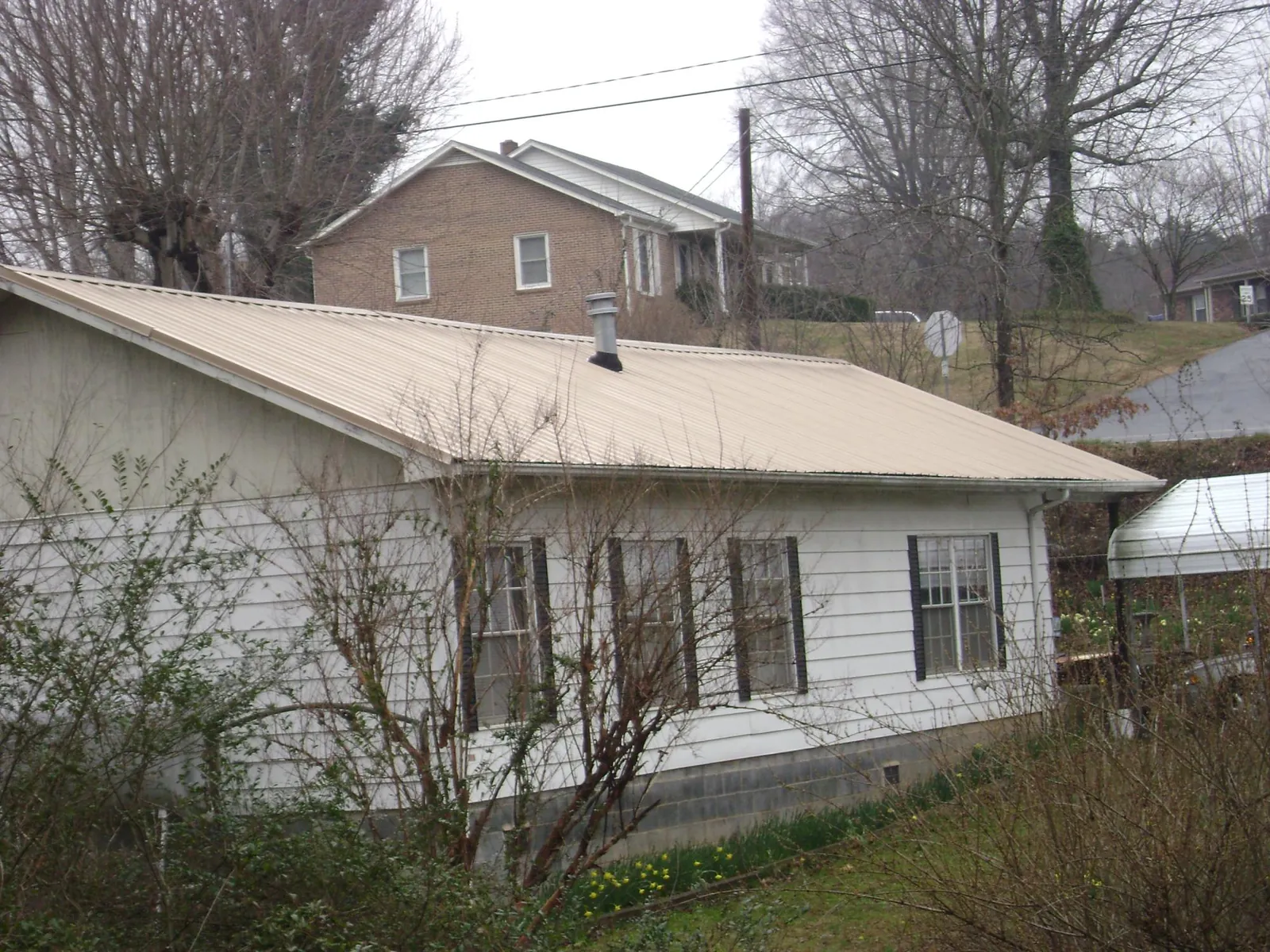 Tan metal roof on a white sided house set into a hillside — Commercial Roofing by Roofing Brothers in White Sulphur Springs